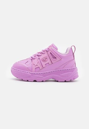 Kraftig lilla sneaker med tyk sål, snørelukning foran og forhøjede dekorative former, herunder en stjerne og et øje på sidepanelet.