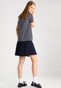 T-shirt a righe navy con maniche corte abbinato a una gonna navy uniforme. La modella indossa scarpe scure e calzini bianchi. Design pulito, vestibilità casual.