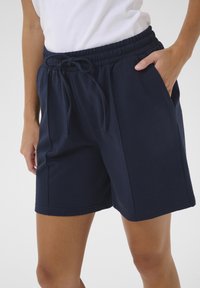 Shorts en coton bleu marine avec une taille élastique et un cordon de serrage. Inclus des poches latérales et une coupe décontractée avec une texture lisse.