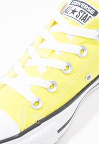 Żółte płócienne trampki z białymi sznurowadłami, gumową osłoną na palcach i srebrnymi oczkami. Posiadają czarno-białe logo na języku oraz czarną podeszwę.