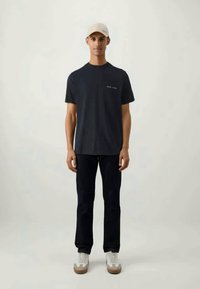 Navy cotton t-shirt with a crew neckline, paired with dark jeans and white sneakers. The model wears a light beige cap. Minimalist design.