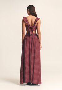 Abito maxi a pois bordeaux con scollatura a V profonda, spalline arricciate e vita legata. Il tessuto sembra leggero e fluente.