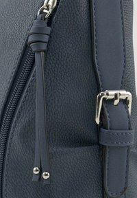 Mørkeblå lædertaske med tekstureret overflade, udstyret med en sølvfarvet lynlås, aftagelig strop og karakteristiske hardware-detaljer.