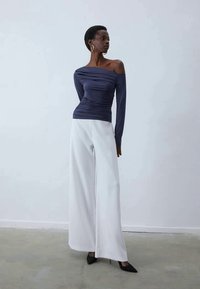 Dolgimi rokavi, off-the-shoulder navy top z gubano teksturo; v kombinaciji s širokimi visokimi belimi hlačami; črne špičaste petke.