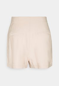 Shorts beige taille haute avec deux poches passepoilées à l'arrière, ourlet droit et détails de couture simples sur un fond clair uni.