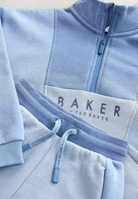 Bluza pentru copii de culoare albastru deschis cu fermoar pe jumătate și pantaloni asortați, prevăzuți cu talie cu șnur și logo-ul "Baker Ted Baker" pe piept.