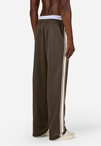 Braune Jogginghose mit lockerer Passform, weißen Seitenstreifen, elastischem Bund und gekrempelten Säumen, kombiniert mit weißen Sneakers.