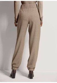 Beige, gemarmerde, high-waisted broeken met een relaxte pasvorm en gathered cuffs, gecombineerd met donkere, hoge laarzen.