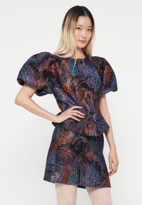 Texturovaný černý textile vrchní díl s živými abstraktními vzory v purpurové a oranžové; vypouklé rukávy; spárované s odpovídajícími rozšířenými sukněmi.