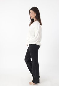 Witte, gestructureerde trui met een losse pasvorm en verlaagde schouders, gecombineerd met zwarte, slim-fit jeans en lichtgekleurde sandalen.