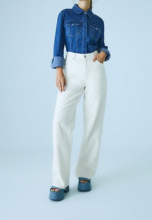 Chemise en jean avec deux poches poitrine, manches retroussées ; pantalon blanc à jambes larges ; chaussures compensées bleues à bouts ouverts ; textures lisses.