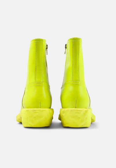 Neon gula ankelstövlar med slätt, glansigt material, gummisula och bakre dragkedjor; rund tå och kraftig, texturerad klack.