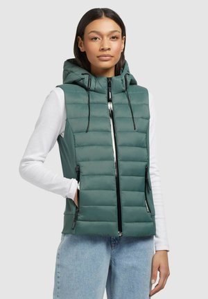 Padded green vest with a hood, featuring a front zipper, side zippered pockets, and a quilted design. Worn over a white long-sleeve shirt.
