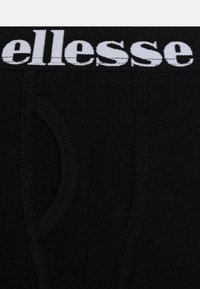 Mutande in cotone nere con un elastico bianco in vita con il logo "ellesse". Texture liscia con dettagli cuciti e apertura frontale.