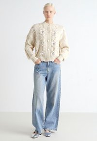 Elfenben kabelstrikket cardigan med knapper, oversized silhuett. Lysblå vid leg jeans med lett slitasje. Sølv slip-on sko fullfører antrekket.