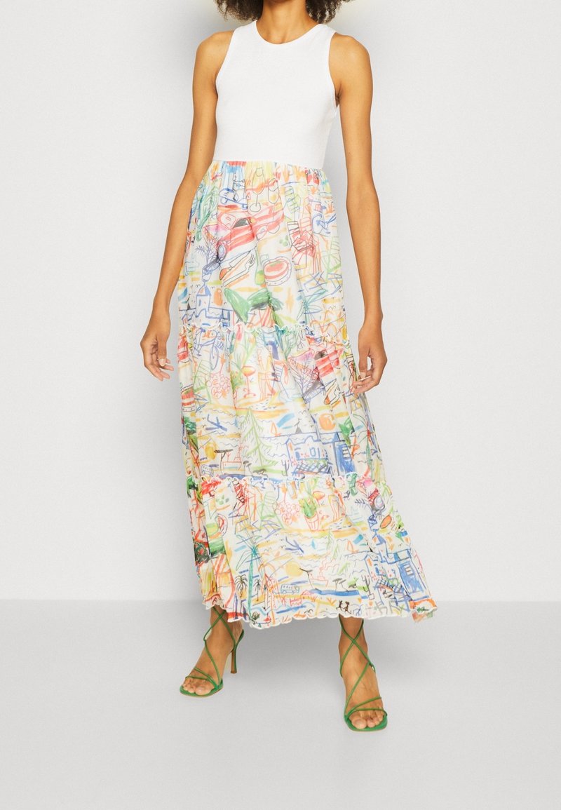 Maxime dress with a fitted white bodice and a layered, colorful patterned skirt featuring abstract drawings; paired with green strappy sandals.