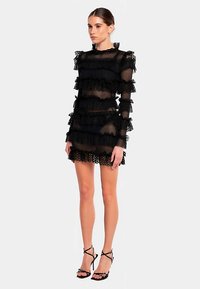 Schwarzes transparentes Kleid mit mehrlagigen Rüschen und floralen Spitzenkanten. Lange Ärmel, figurbetonte Silhouette und ein geraffter Halsausschnitt.