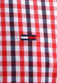 Tela a cuadros roja y blanca con detalles en azul marino. Cuenta con un pequeño logo bordado con rayas rojas, blancas y azules en el centro.