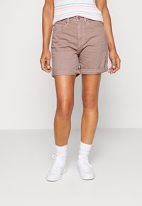 Pantalones cortos de mezclilla marrón claro con dobladillos enrollados, diseño de cinco bolsillos y cierre de botón, combinados con zapatillas blancas y calcetines.