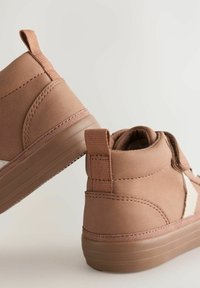 Chaussures à capuche marron avec une texture lisse, dotées d'une semelle en caoutchouc beige, d'un panneau latéral blanc contrastant et d'une languette à l'arrière pour un enfilage facile.
