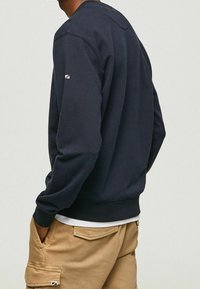 Navy blue sweatshirt in cotton blend, featuring ribbed cuffs and hem. Small logo accent on left sleeve. Relaxed fit with crew neckline.