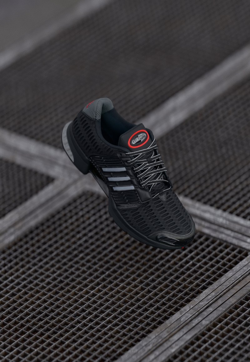 Chaussure de sport noire avec une tige en maille, des côtés texturés et des accents réfléchissants ; dispose de lacets gris et d'un logo rouge proéminent.