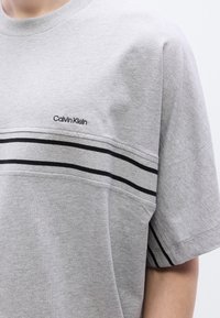 Γκρι βαμβακερό t-shirt με στρογγυλή λαιμόκοψη, κοντά μανίκια και μαύρες οριζόντιες ρίγ ες στο στήθος. Κεντημένο λογότυπο στο μπροστινό μέρος.