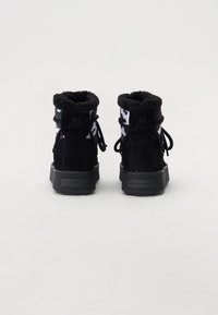 Botas de tobillo de ante negro con una suela texturizada negra, cuello forrado de piel sintética y un patrón de camuflaje en los lados superiores. Cierre de cordones ajustable.