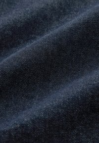 Mørkeblå denimstof med en glat tekstur, der har en let glans og et subtilt diagonalt vævemønster.