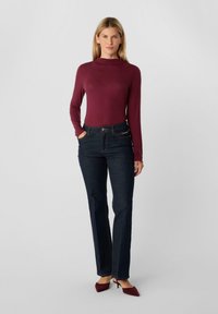 Bordowa bluzka z długim rękawem w zestawieniu z ciemnoniebieskimi prostymi jeansami. Charakterystyczne detale to zapięcie na guziki i suwak w spodniach.