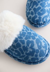 Chaussons bleus à motifs avec doublure blanche et duveteuse, présentés en gros plan sur une surface neutre.