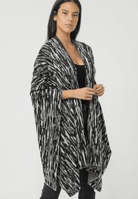 Chal negro y blanco con estampado, de frente abierto, con mangas anchas y una textura suave. La tela ligera cae de manera elegante.