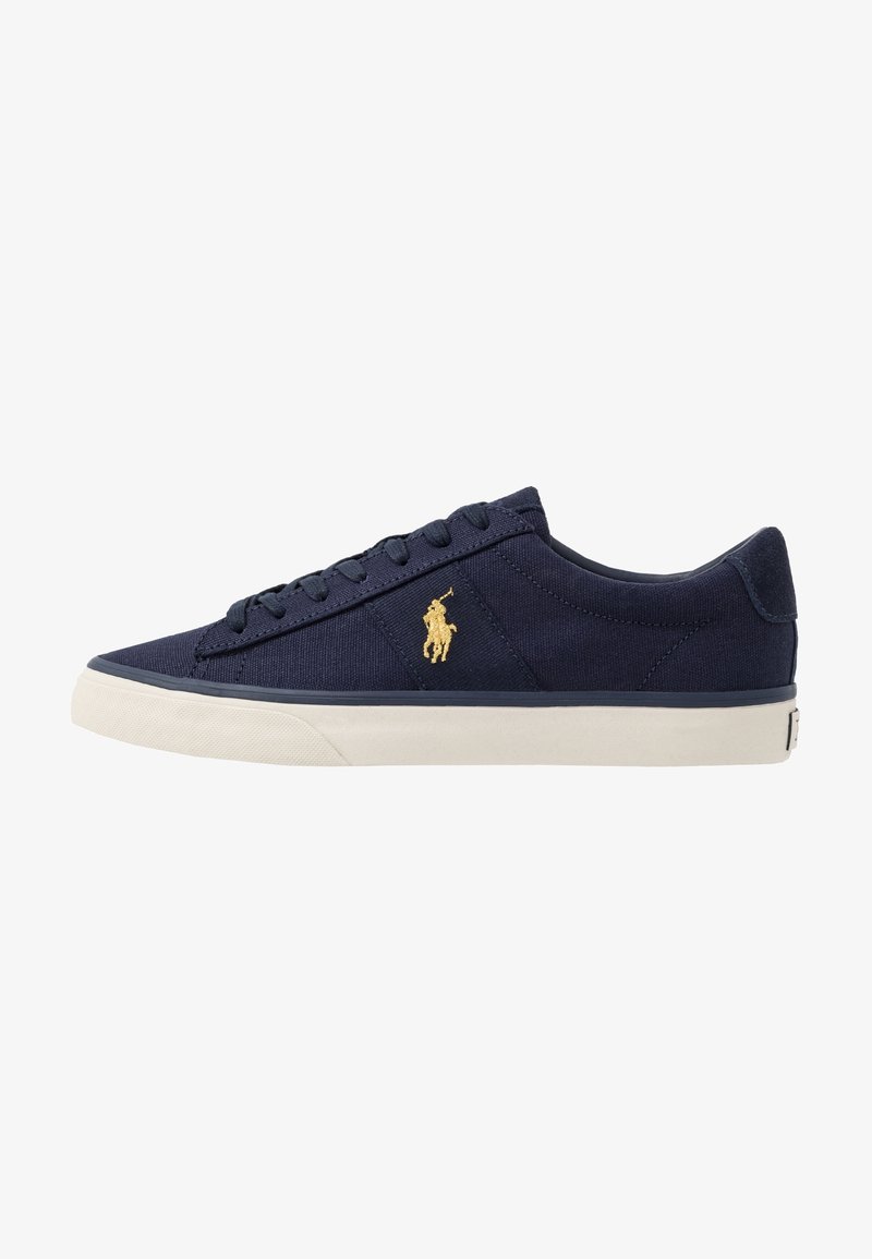 Marineblauwe canvas sneaker met een witte rubberen zool, voorzien van ronde veters en een gouden polo-logo aan de zijkant. Glad oppervlak en een laag profiel ontwerp.