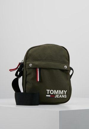 Olijfgroene Tommy Jeans crossbodytas met een zwarte verstelbare band, een voorklepvak en een rood, wit en blauw ritstrekkerlabel.