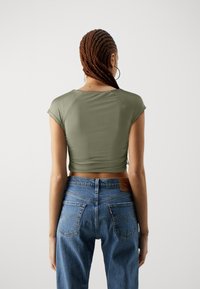 Top aderente verde oliva a maniche corte con scollatura rotonda, abbinato a jeans in denim blu a vita alta con un design classico della tasca posteriore.