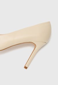 Scarpa con tacco alto beige con tomaia in pelle liscia, punta appuntita e un sottile accento metallico sul tallone. Design minimalista con linee eleganti.