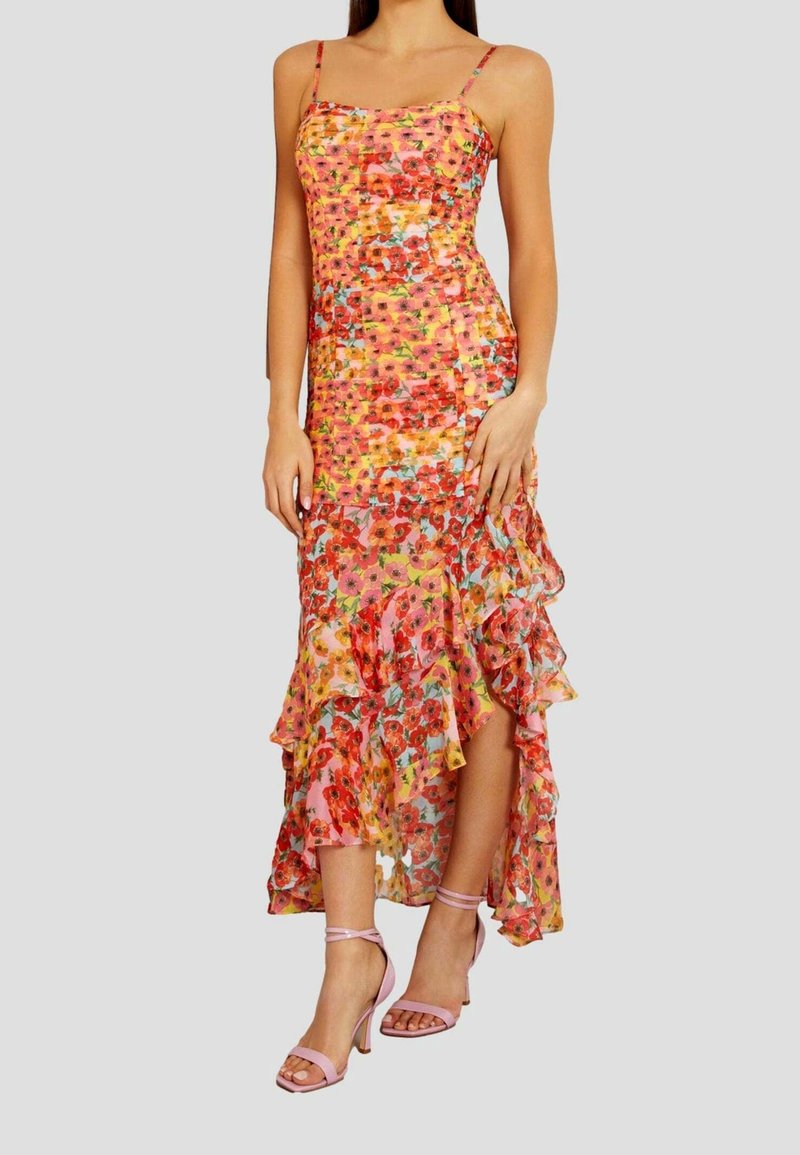 Robe maxi florale avec bretelles spaghetti, ourlet volé, couleurs vives de rose, orange et bleu. Portée avec des talons roses à lanières.