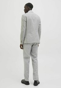 Traje de cuadros en gris claro con una silueta ajustada. Tejido texturizado, con una abertura central en la parte trasera, y zapatos negros completan el conjunto.
