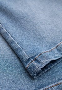 Denim-kangas vaaleansinisinä, hienovaraisella tekstuurilla ja kontrastoivalla ruskealla ommella reunoilla ja saumoissa. Huolellisesti taitettu.