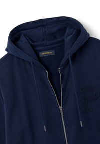 Sudadera con cremallera de color azul marino, hecha de un tejido suave, cuenta con una capucha, una cremallera frontal y la letra "P" bordada en el lado izquierdo. La etiqueta dice "PIOMBO".