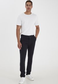 T-shirt bianca a maniche corte abbinata a pantaloni slim-fit blu scuro e sneakers bianche, con una texture di tessuto liscia e un design classico.