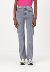 High-waisted, light blue denim jeans with a straight fit, featuring front pockets and a button closure. Pairing with gray sneakers.