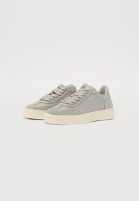 Adidași gri cu un exterior din piele netedă și suede texturat, vârf rotund, sistem de închidere cu șnururi cu șase ochiuri și o talpă groasă din cauciuc alb-crem.