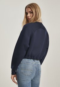 Felpa cropped blu navy con maniche lunghe, polsini a coste e orlo elastico; abbinata a jeans azzurri con tasche posteriori.