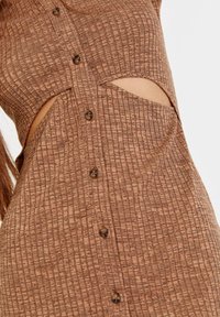 Hnědé šaty s vzorem, které mají knoflíkové zapínání, výřezy a strukturovanou látku s mřížkovým designem.