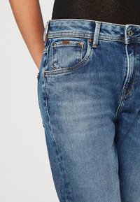 Light blue denim jeans featuring a fitted design, contrasting stitching, five-pocket style, and a brown logo label on the back pocket.