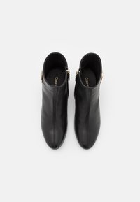 Stivali alla caviglia in pelle nera con un design elegante, dotati di una cerniera laterale e dettagli in metallo dorato. Texture liscia con punta affilata.