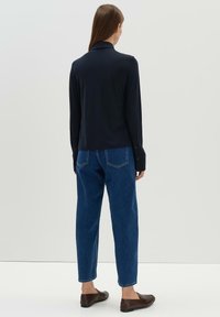 Navy long-sleeve shirt with a collar, paired with blue high-waisted jeans. Dark brown flat shoes. Simple design, smooth texture.