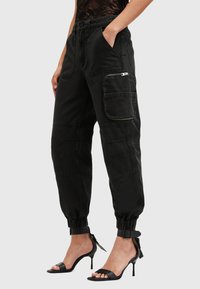 Zwarte cargobroek met een losse pasvorm, elastische manchetten, zijzakken en ritszakdetails. Gemaakt van duurzaam materiaal met een matte textuur.