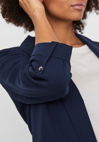 Mörkblå skjorta med upplockad ärm, med en knappdetalj. Mjuk, slät tygtextur, med en enkel design och rundad halsringning.